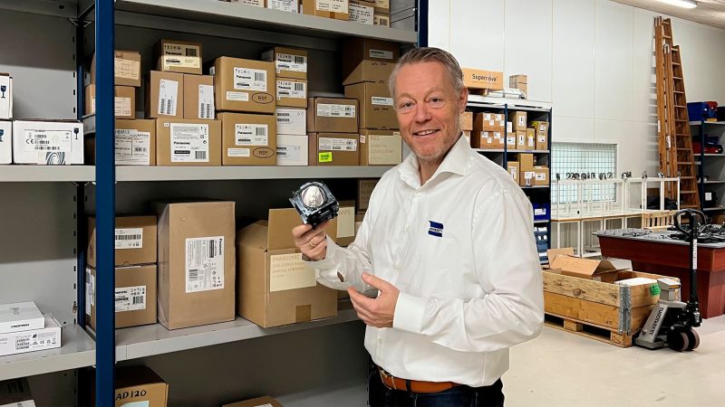 Mand står i lagerlokale med projektorlampe i hånden