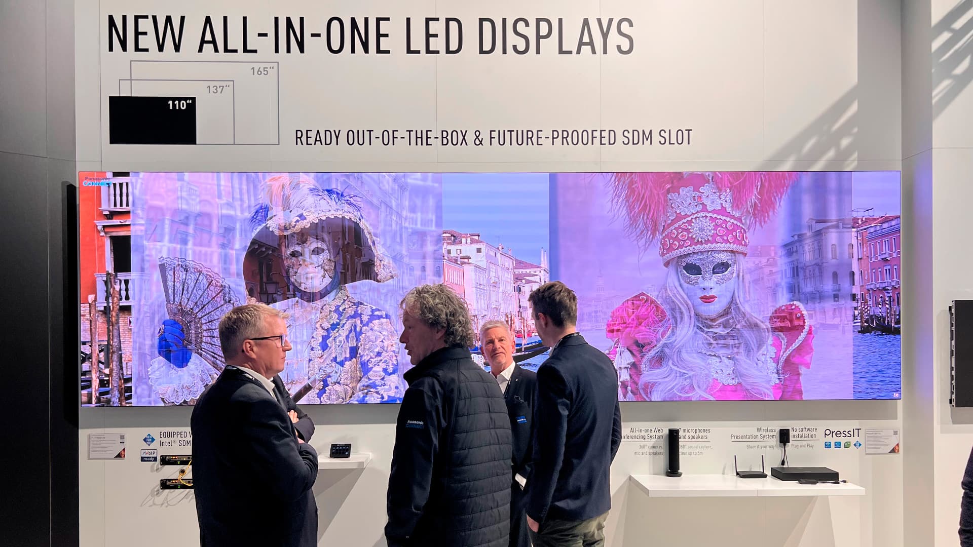 Panasonic messestand med LED skærme på væg og mennesker i samtale foran